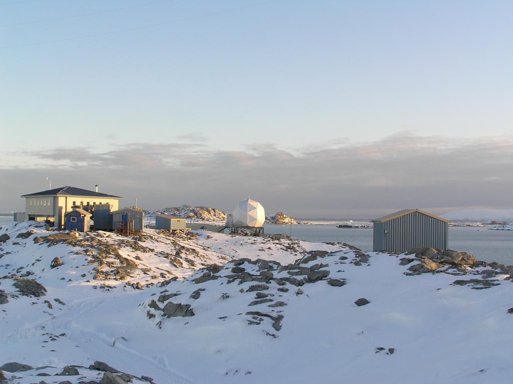 Buildings amidst the snow and rock to form a research station. A large white ball-type object is in the center.