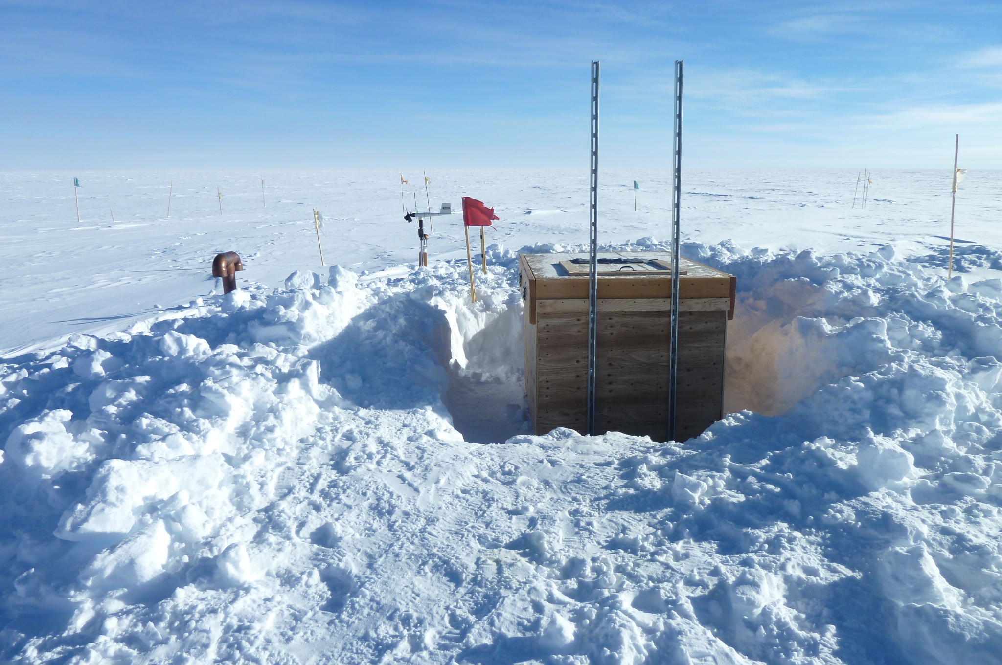 A wooden box amongst flags and poles surrounded by snow. 